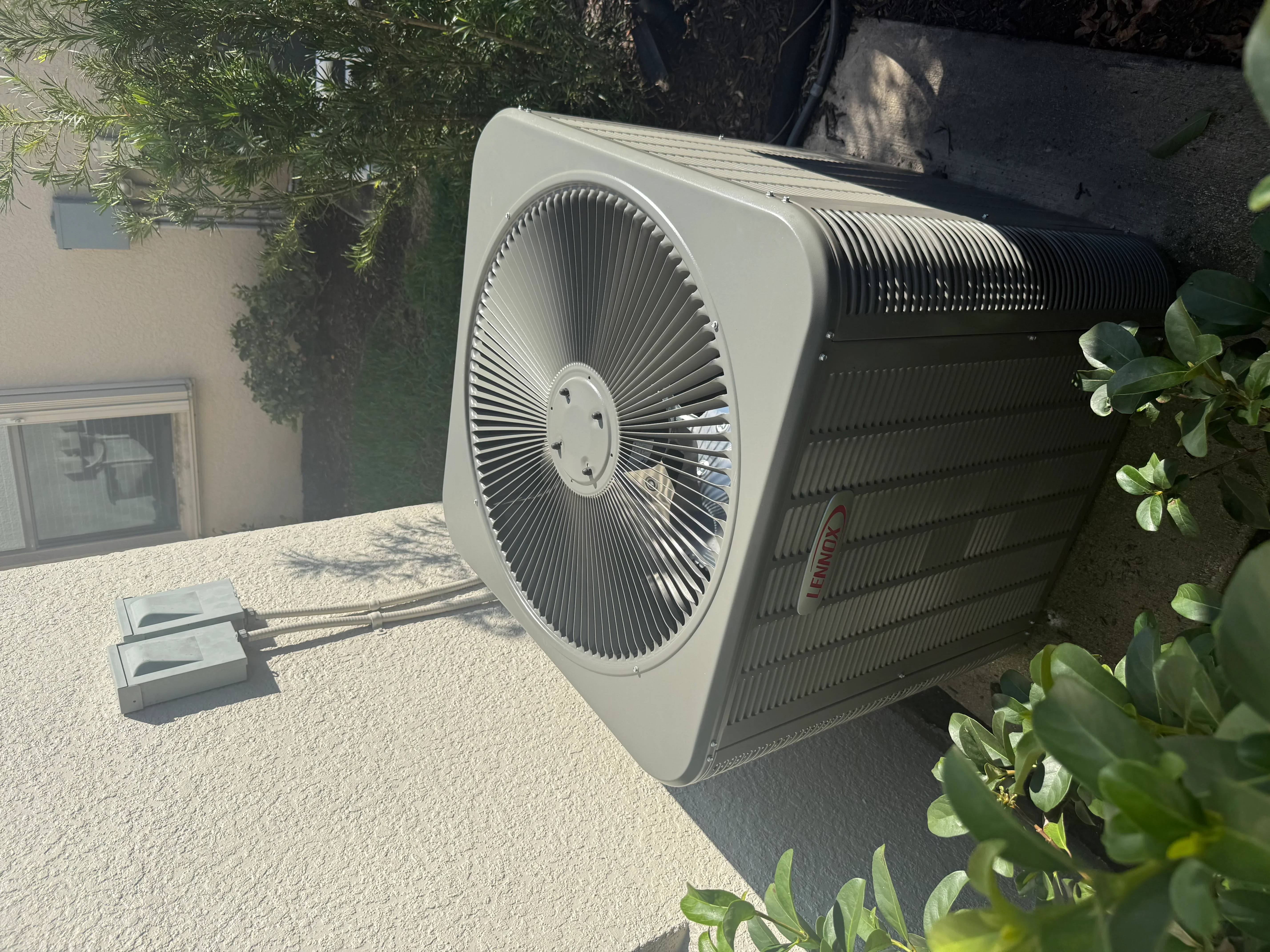 White heat pump unit installed on concrete pad with black ducting and electrical connections