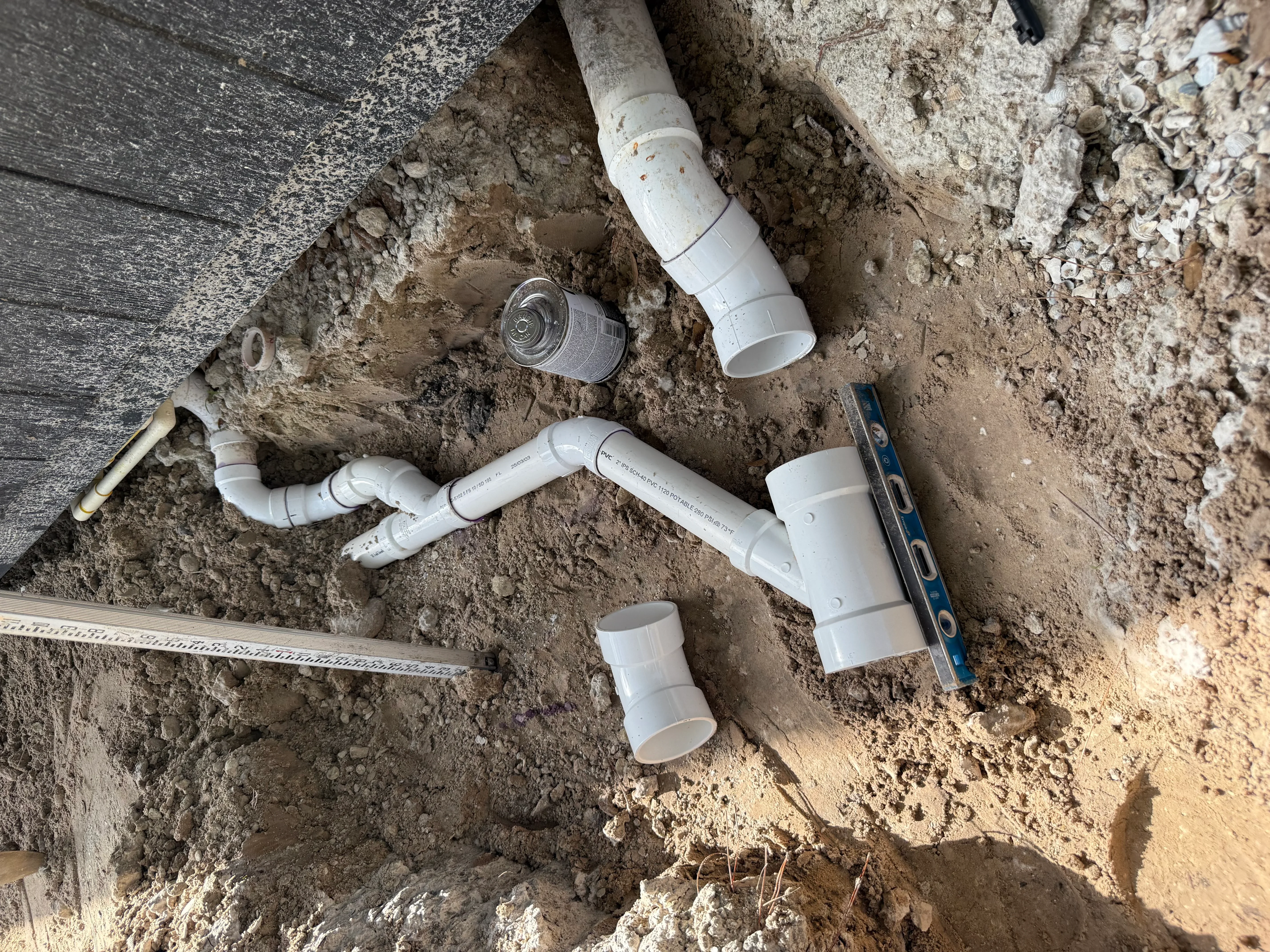 White PVC drainage pipes and fittings installed in underground trench with soil excavation