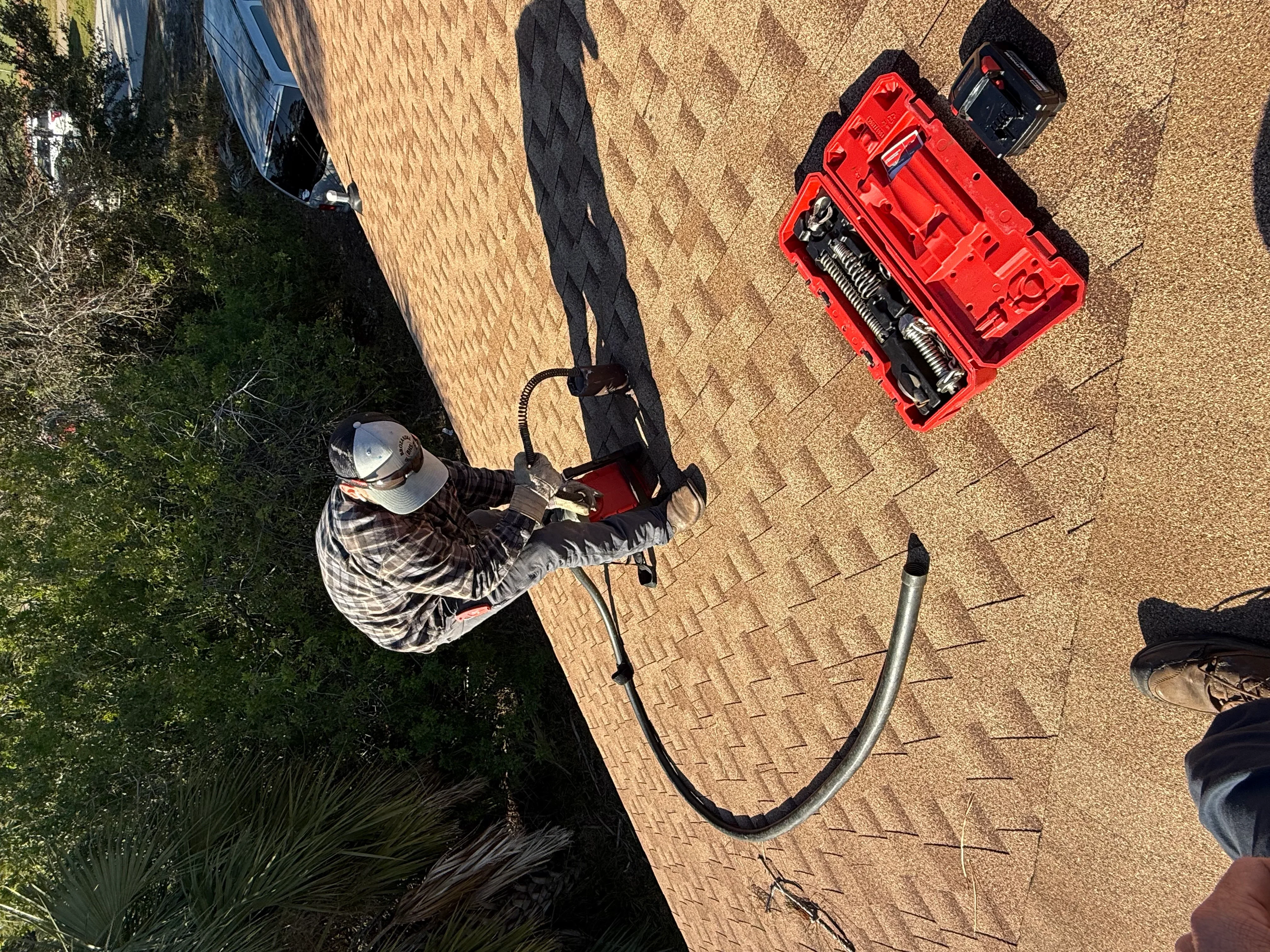 Plumber with red toolbox performing residential plumbing service on brick driveway