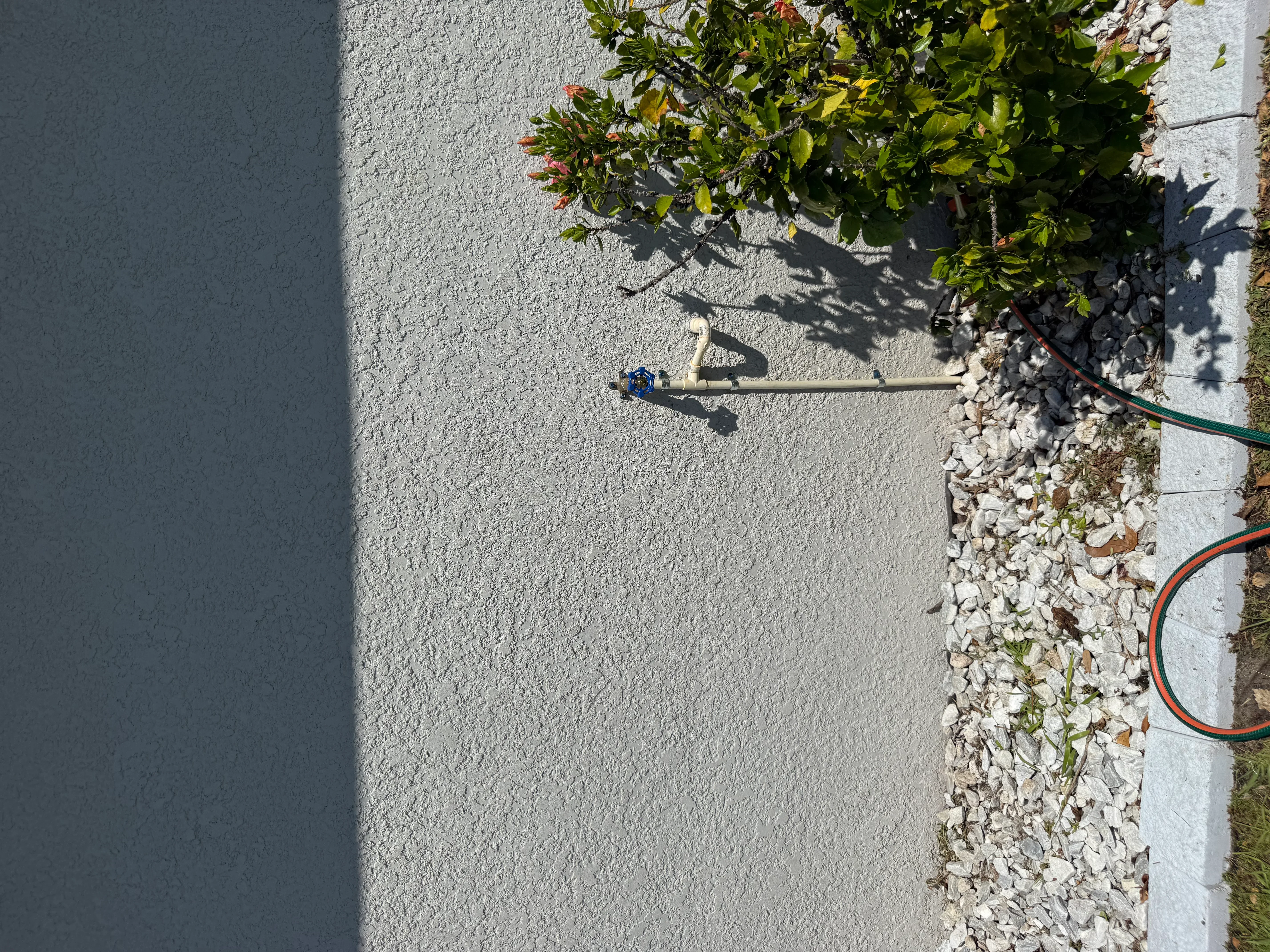 Outdoor irrigation system with blue sprinkler head, green and orange hoses, white stone mulch border